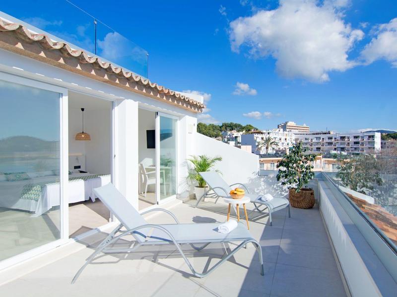 Terrasse sur le toit lumineuse avec chaises longues blanches, vue sur la ville et la mer.