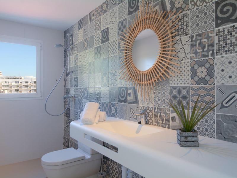 Salle de bain lumineuse avec carrelage décoré, miroir rond et toilettes modernes.