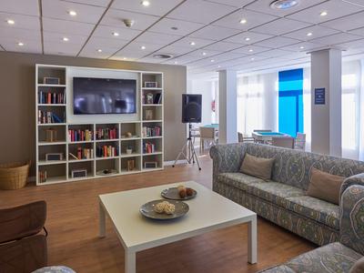Gemütliches Wohnzimmer mit Bücherregal, Fernseher, Couchtisch und Sofas in einem Hotelzimmer.