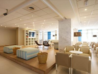 Heller, moderner Hotel-Loungebereich mit Sesseln, Sofas und großen Fenstern.