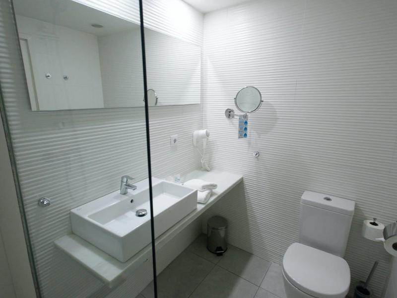 Bagno moderno con lavabo, specchio, asciugacapelli e WC in colori neutri.