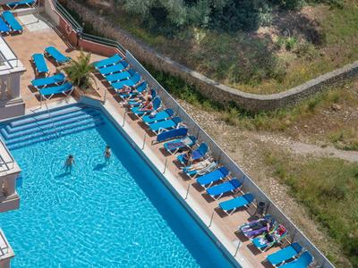 Hotelpool mit blauen Liegen an der Seite und Gästen im Wasser und auf den Liegen.