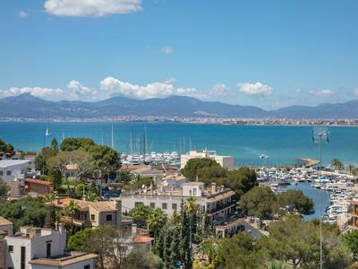 Blick auf eine Küstenstadt mit Yachthafen, Gebäuden und Bergen im Hintergrund.