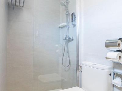 Baño moderno y luminoso con ducha de vidrio, inodoro blanco y toallero.