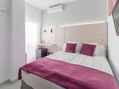 Habitación de hotel compacta con cama doble, paredes blancas, escritorio y TV de pared.