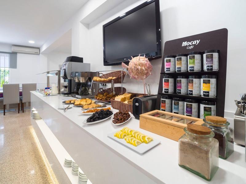 Buffet avec café, thé et pâtisseries dans une salle à manger d'hôtel lumineuse.