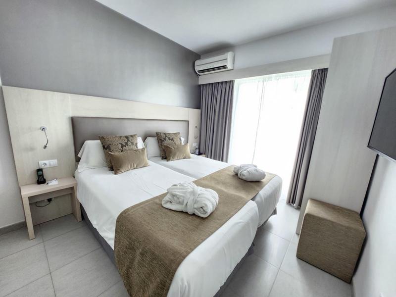 Chambre d'hôtel moderne avec deux lits, accents bruns, balcon, lumineuse et confortable.