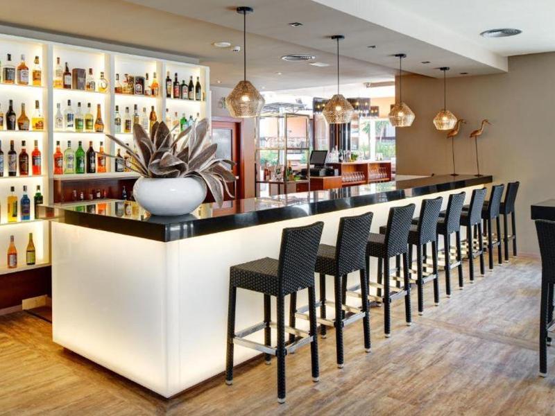 Moderner Barbereich mit beleuchtetem Tresen, schwarzen Barhockern und Holzfußboden.