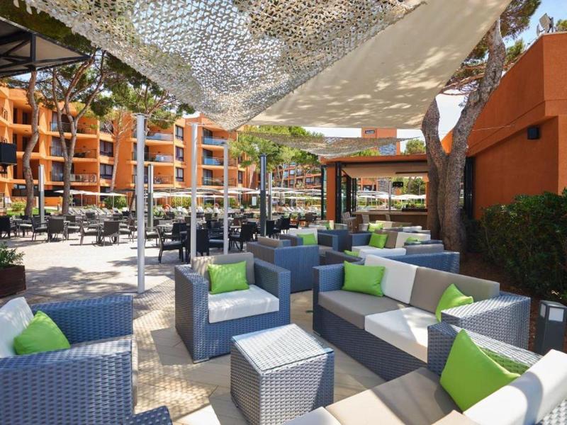 Outdoor-Lounge mit grauen Sitzmöbeln, grünen Kissen und schattenspendendem Netz über dem Sitzbereich.