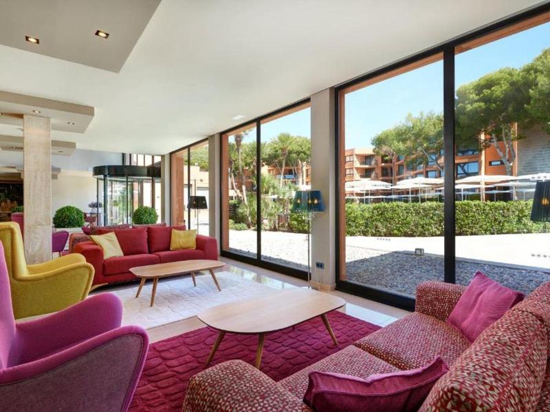 Helles Wohnzimmer mit großen Glasfenstern, bunten Sesseln und Sofas, rotem Teppich und modernem Ambiente.