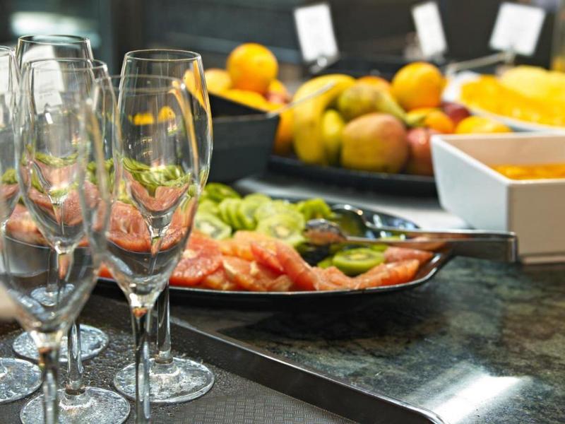 Drei leere Weingläser stehen vor einem Teller mit aufgeschnittenem Obst auf einer schwarzen Oberfläche.