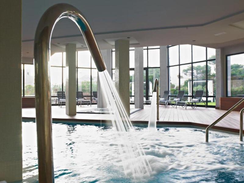 Innenpool mit Edelstahl-Wasserdüse, breiter Fensterfront und Treppe, Wasser fließt ins Becken.