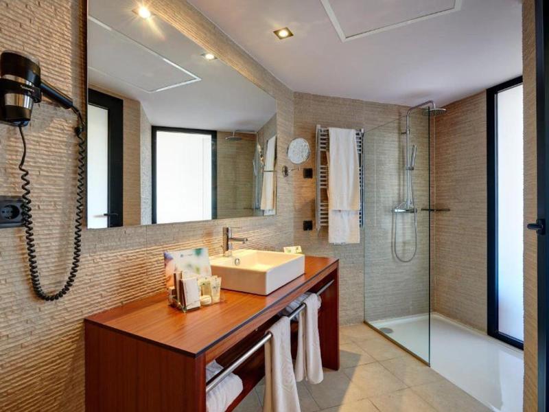 Helles Badezimmer mit Glas-Dusche, großem Spiegel, Holzwaschtisch und beige Wandfliesen.