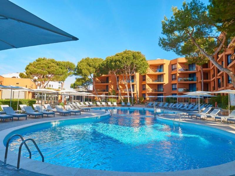 Schwimmbad mit blauer Wasseroberfläche, Sonnenschirmen und mehrstöckigem Hotel im Hintergrund.