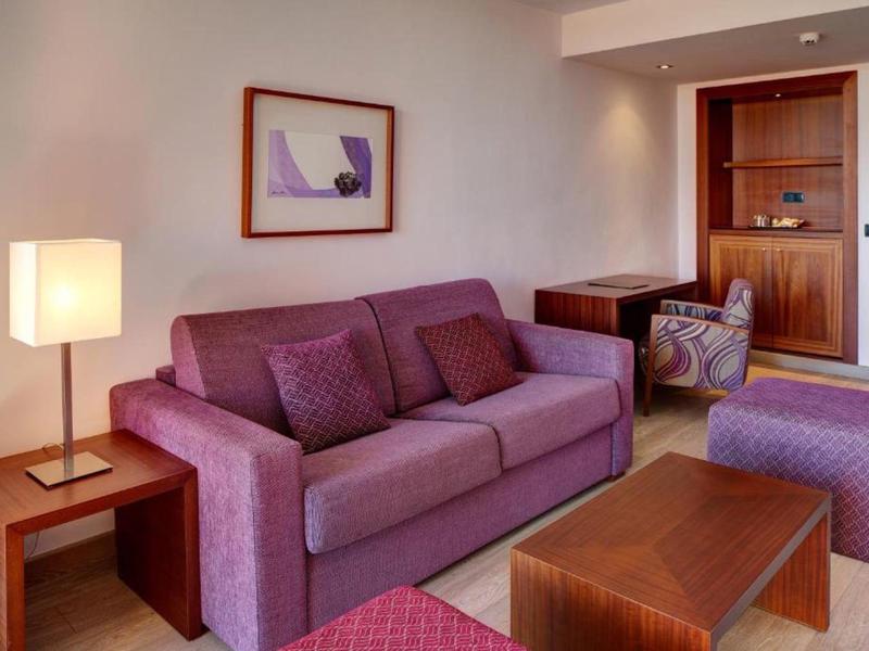 Modern eingerichtetes Wohnzimmer mit lila Sofa, Holztisch, Stehlampe und einem Bild an der Wand.