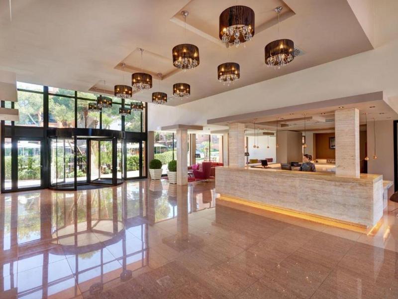 Großer, heller Hotellobby mit glänzendem Boden, modernen Lampen und Empfangstresen aus Stein.