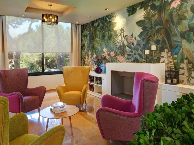 Gemütliches Wohnzimmer mit bunten Sesseln, großem Fenster und exotischer Dschungel-Wandmalerei.