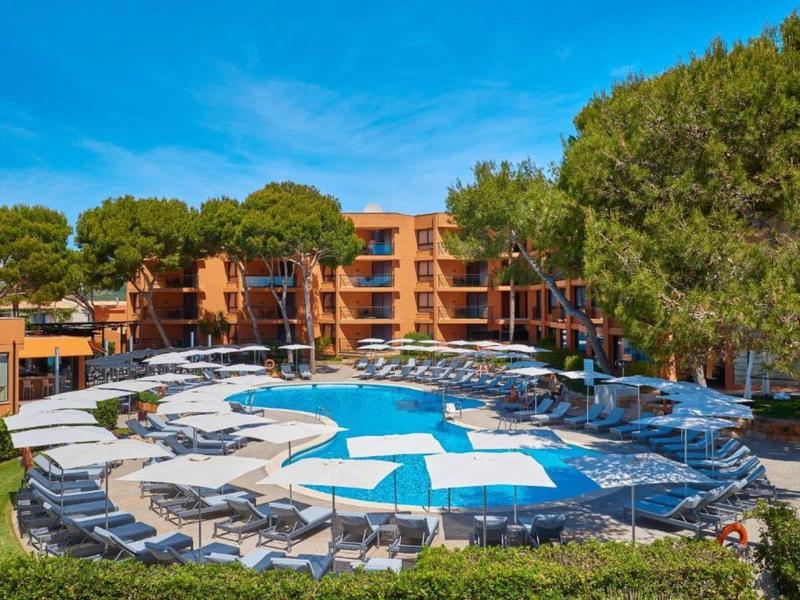 Moderner Hotelpool mit Liegestühlen und Sonnenschirmen inmitten von Bäumen und blauem Himmel.
