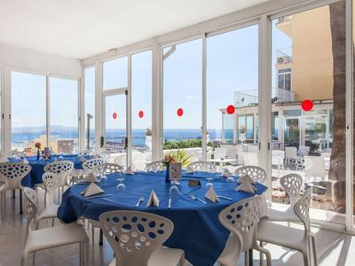 Jasna jadalnia z niebieskimi obrusami i widokiem na morze przez duże okna.