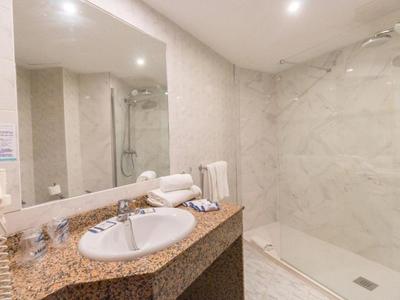 Elegantní koupelna s mramorovými dlaždicemi, velkým zrcadlem a moderní sprchou.