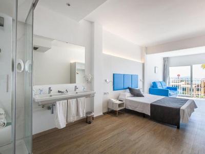 Moderní hotelový pokoj s manželskou postelí, televizí, otevřenou koupelnou a balkonem s výhledem na moře.