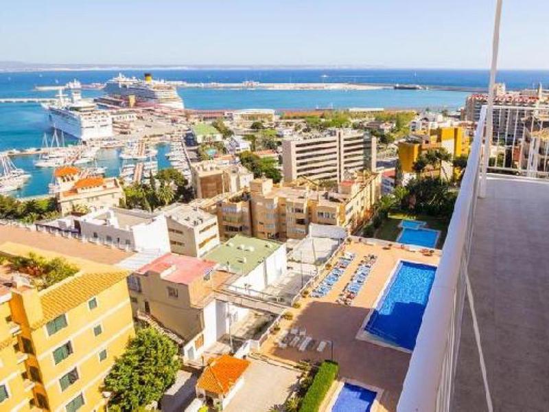 Výhled na přístav s výletními loděmi, městskými budovami a přímořským bazénem.