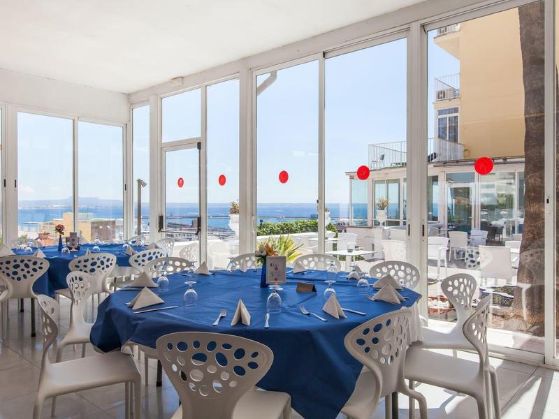 Elegantní restaurace s modrými ubrusy a velkými okny s výhledem na moře.