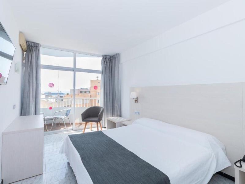 Moderní hotelový pokoj s velkým oknem, manželskou postelí a posezením s židlí a stolem.