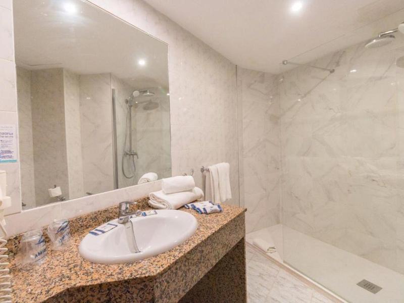 Elegantní koupelna s mramorovými dlaždicemi, velkým zrcadlem a moderní sprchou.