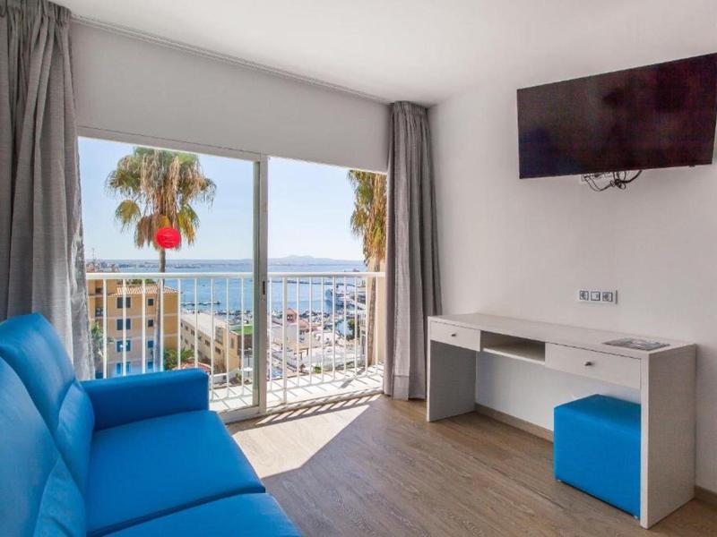 Světý pokoj s modrou pohovkou, psacím stolem a výhledem na moře přes velká okna.