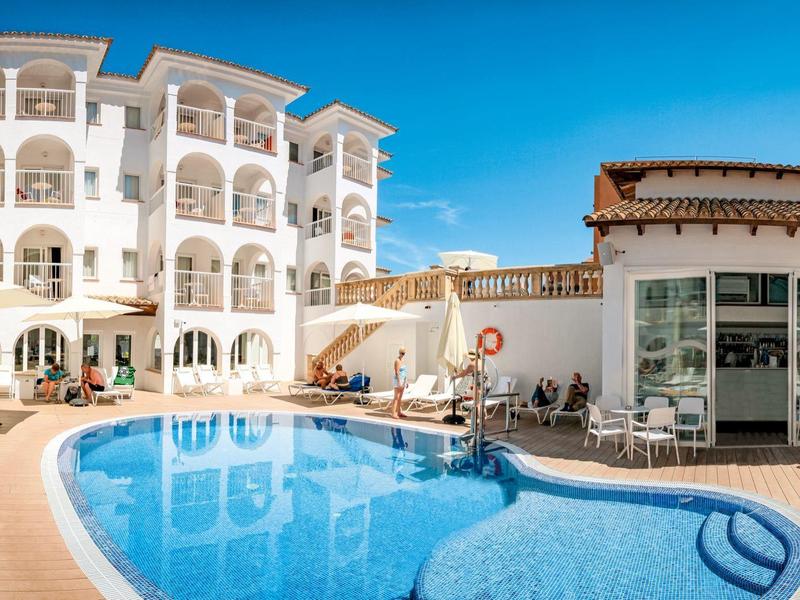 Hotel met groot zwembad, ligstoelen en heldere blauwe lucht.