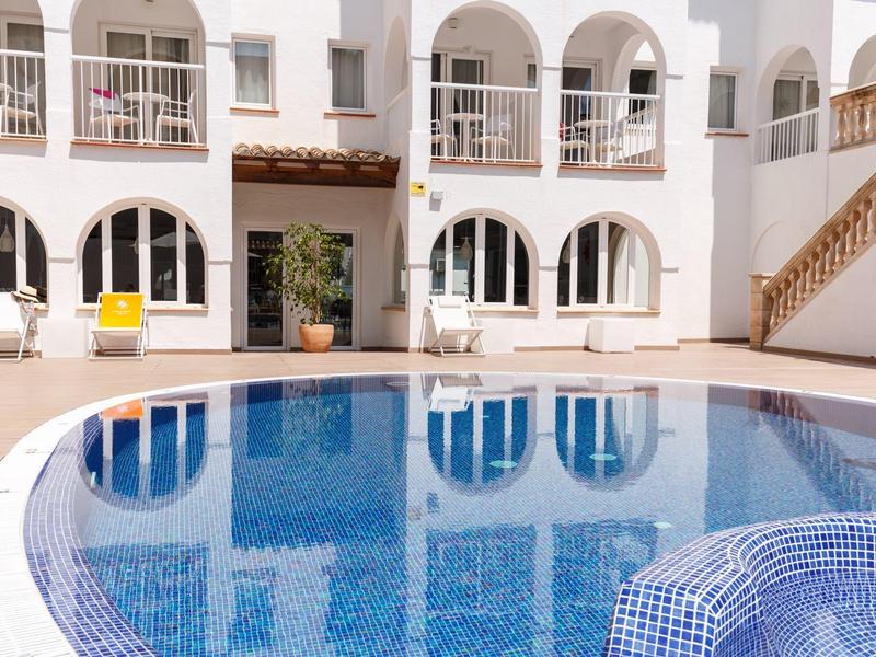 Binnenplaats met blauw zwembad en wit gebouw met bogen en balkons.