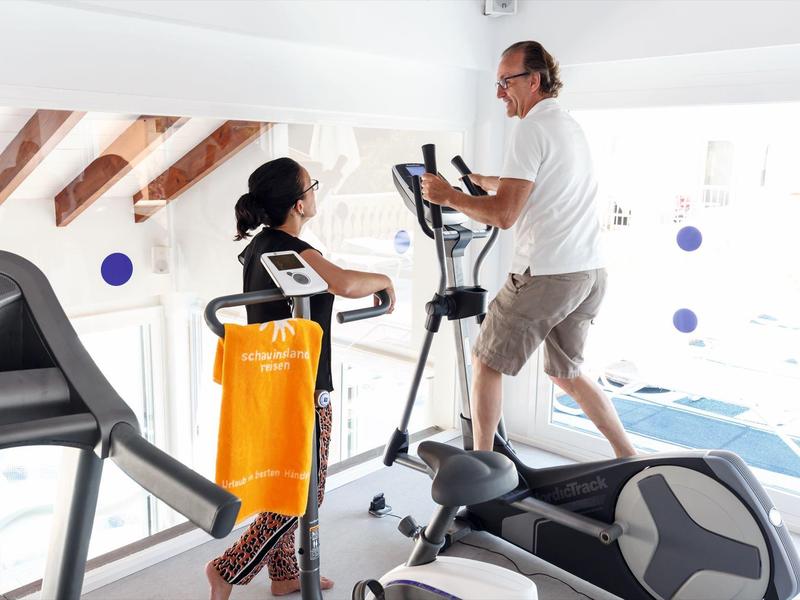 Twee mensen sporten samen op een crosstrainer in een lichte fitnessruimte met houten balken.