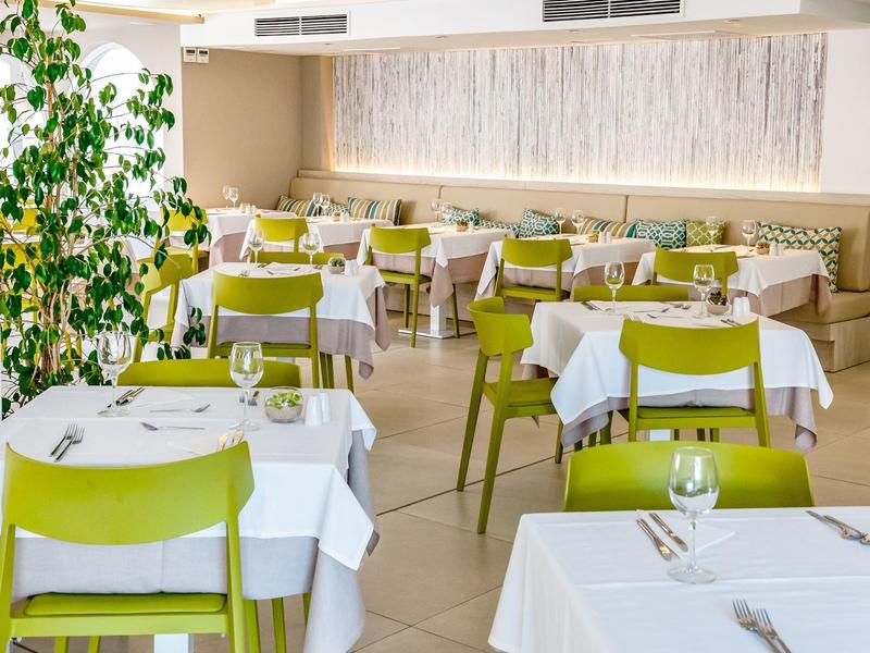 Lichte, moderne eetzaal met witte gedekte tafels en groene stoelen in een hotel.