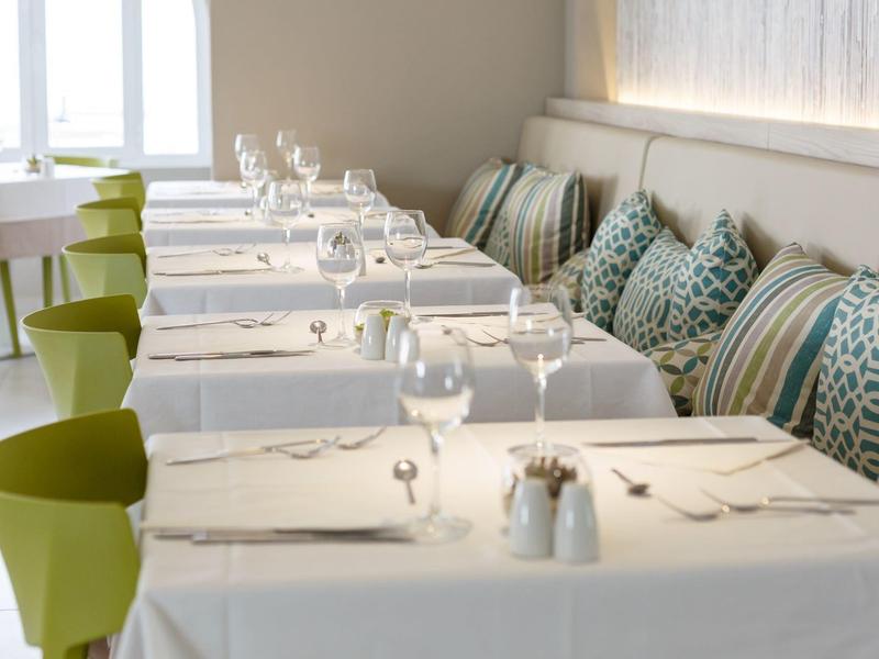 Elegant restaurant met witte tafelkleden, groene stoelen en decoratieve kussens langs de muur.