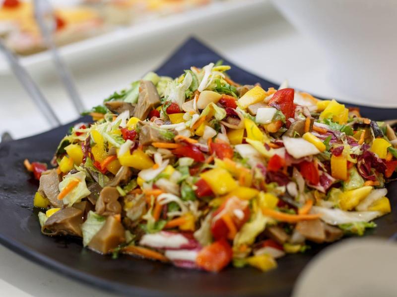 Kleurrijke salade met paprika, cornflakes en andere ingrediënten op een zwart bord.