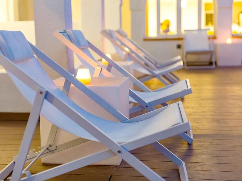 Lege witte ligstoelen op houten vloer voor een fel verlicht gebouw.