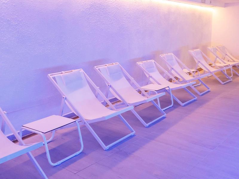 Rij witte ligstoelen tegen een lichtpaarse muur met zachte verlichting.