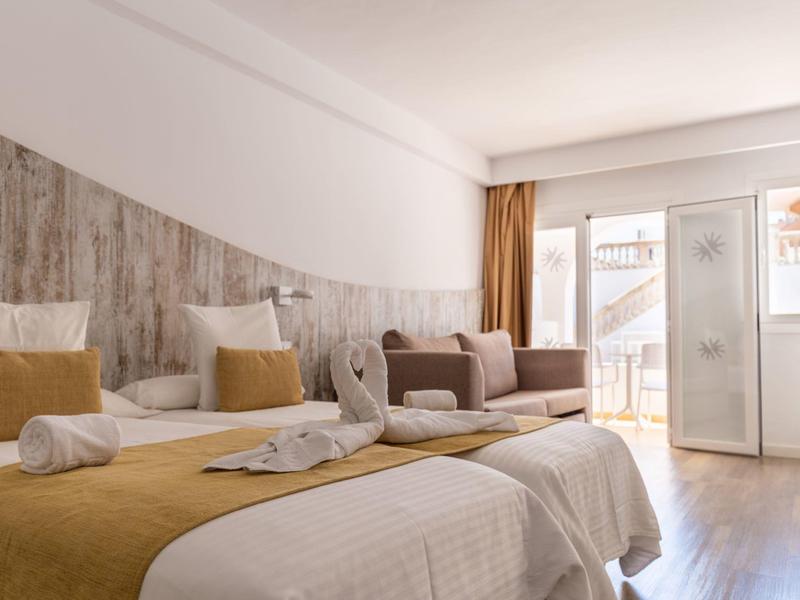 Lichte hotelkamer met twee bedden, decoratief gevouwen handdoeken en balkon met zeezicht.