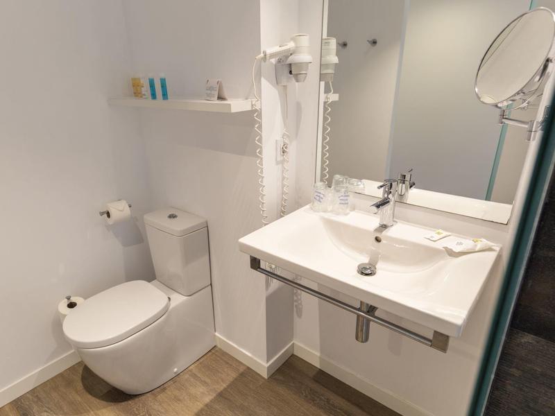 Kleine moderne badkamer met toilet, wastafel, grote spiegel en witte muren.