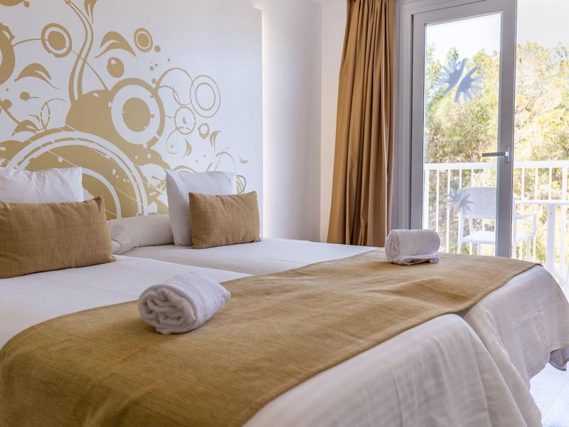 Licht ingericht hotelkamer met tweepersoonsbed en balkon met uitzicht op palmbomen.