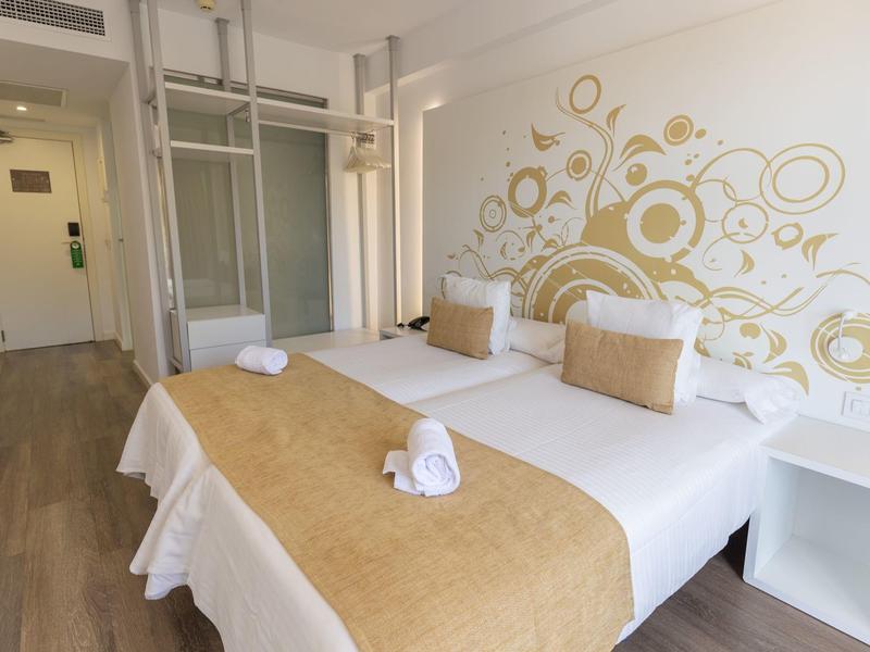 Lichte hotelkamer met twee eenpersoonsbedden, gouden accenten en modern design.