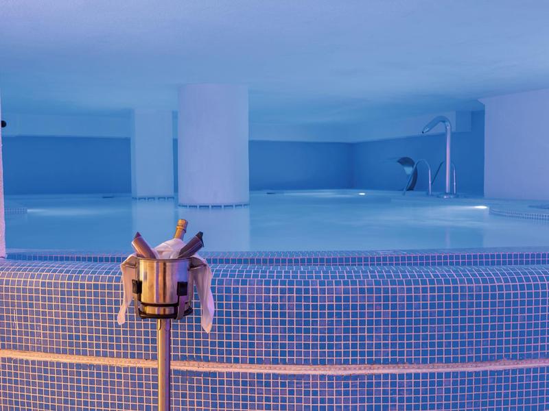 Moderne binnenzwembad met mozaïektegels en een houten thermometer aan de muur.