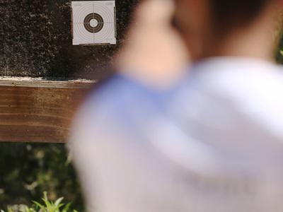Ein schießender Junge zielt auf eine Zielscheibe mit schwarzem Punkt auf weißem Hintergrund.