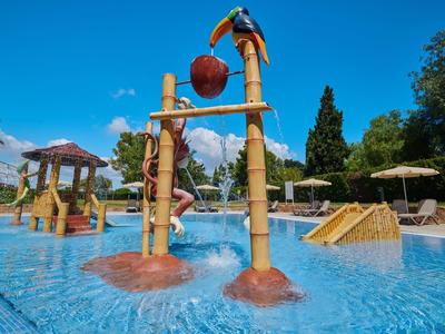 Wasserpark mit bunten Spielgeräten, Palmen, Sonnenschirmen und klarem blauem Wasser.