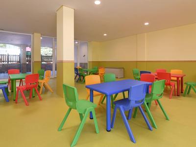 Bunter Kindergartenraum mit kleinen Tischen und Stühlen aus Kunststoff auf gelbem Boden.