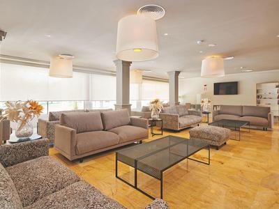 Heller, moderner Wohnraum mit großen Fenstern, hellgrauen Sofas, Glastischen und Holzfußboden.