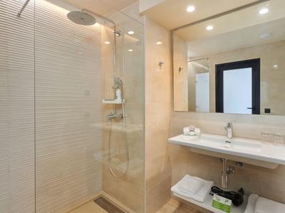 Modernes Badezimmer mit begehbarer Dusche, großem Spiegel, Waschbecken und weißen Handtüchern.