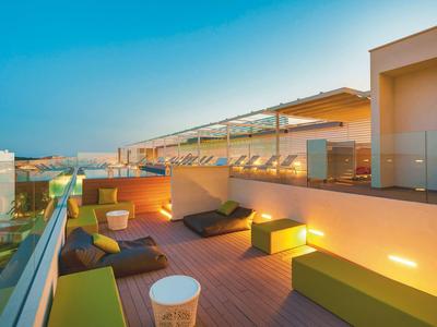 Dachterrasse mit moderner Sitzmöbelgruppe, Holzterrasse und Glasgeländer bei Sonnenuntergang.