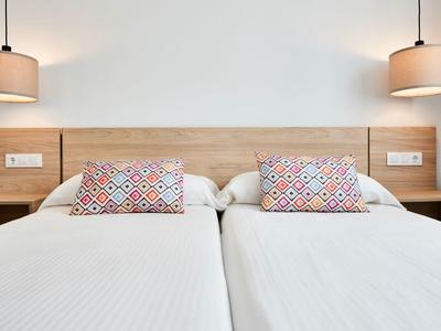 Twee eenpersoonsbedden met wit beddengoed en kleurrijke kussens, geflankeerd door houten nachtkastjes en hanglampen.